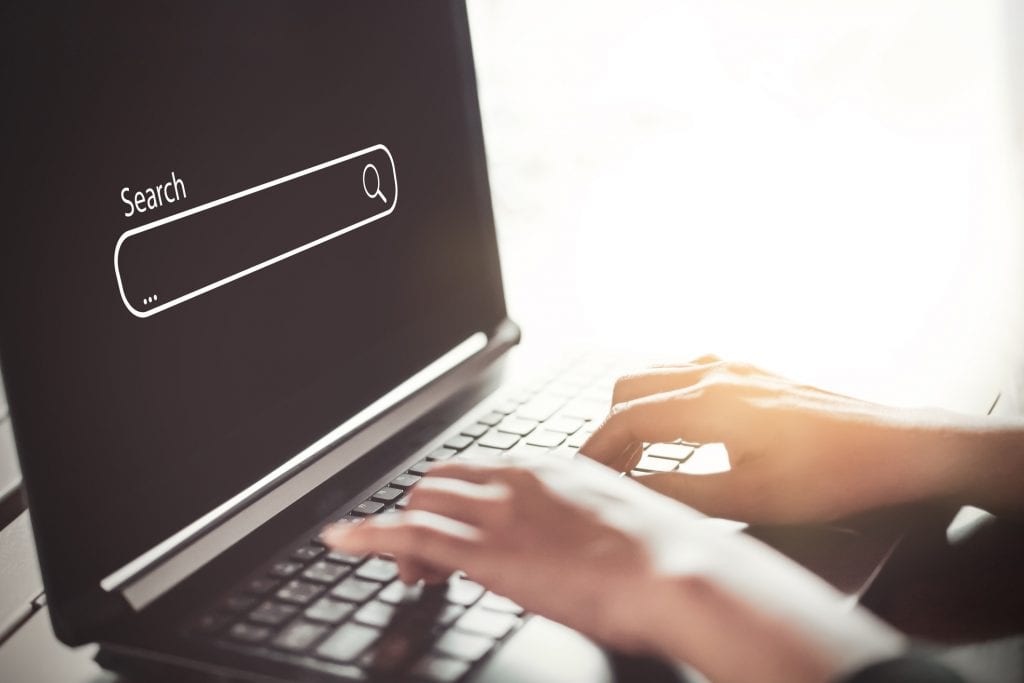 Woman hand using keyboard laptop with search bar icon on screen at coffee shop. Business technology and freelance concept. Vintage tone filter effect color style.