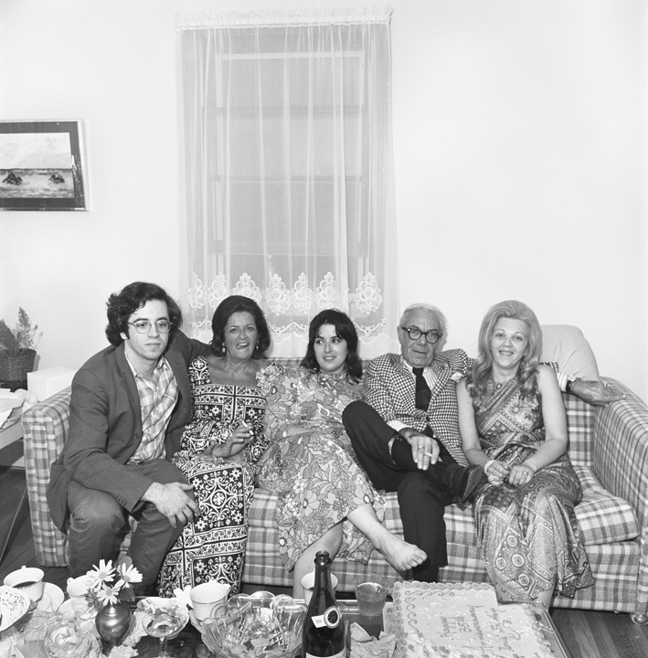 A black and white family photograph of five people in formal attire sitting on a plaid sofa.