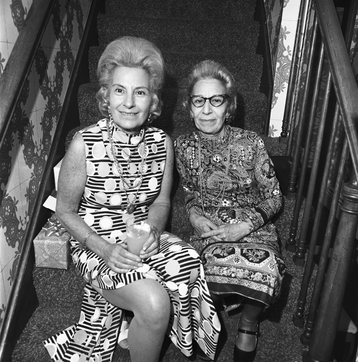 A black and white photograph of two older women sitting on the stairs and posing for a picture.