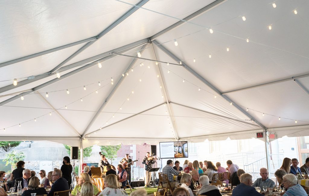 A group of people dining under a tent listening to a group of musicians.