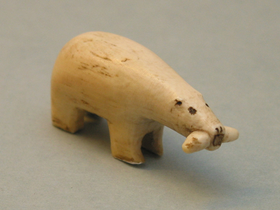 A miniature carving of a polar bear with a fish in it's mouth made of Walrus ivory.