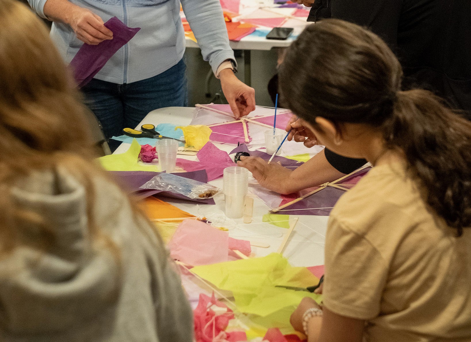 People making colorful paper kites at a workshop table.