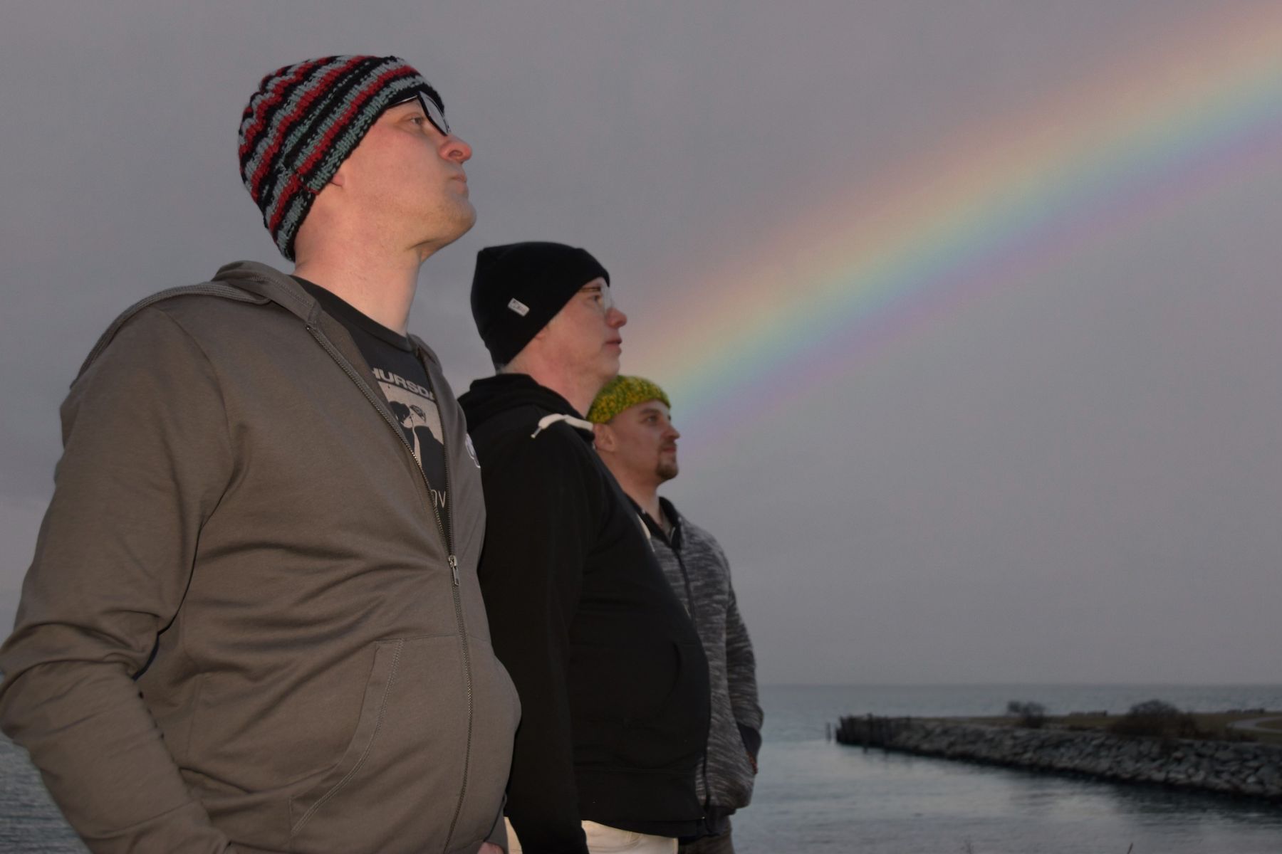 Scapeghost Three men standing by the water under a rainbow.