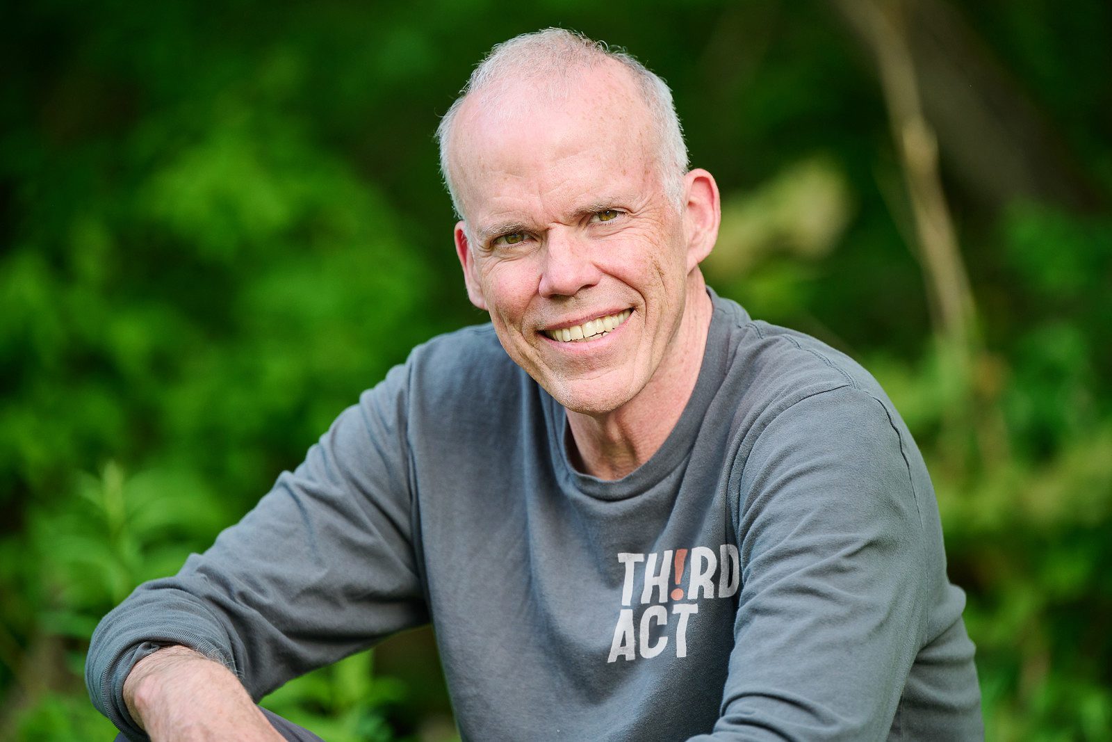Bill McKibben Portrait of Bill McKibben smiling outdoors in a gray Third Act shirt.