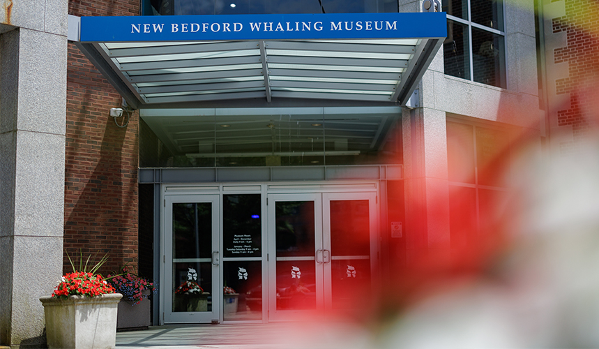 Entrance to the New Bedford Whaling Museum with glass doors and a blue sign overhead.