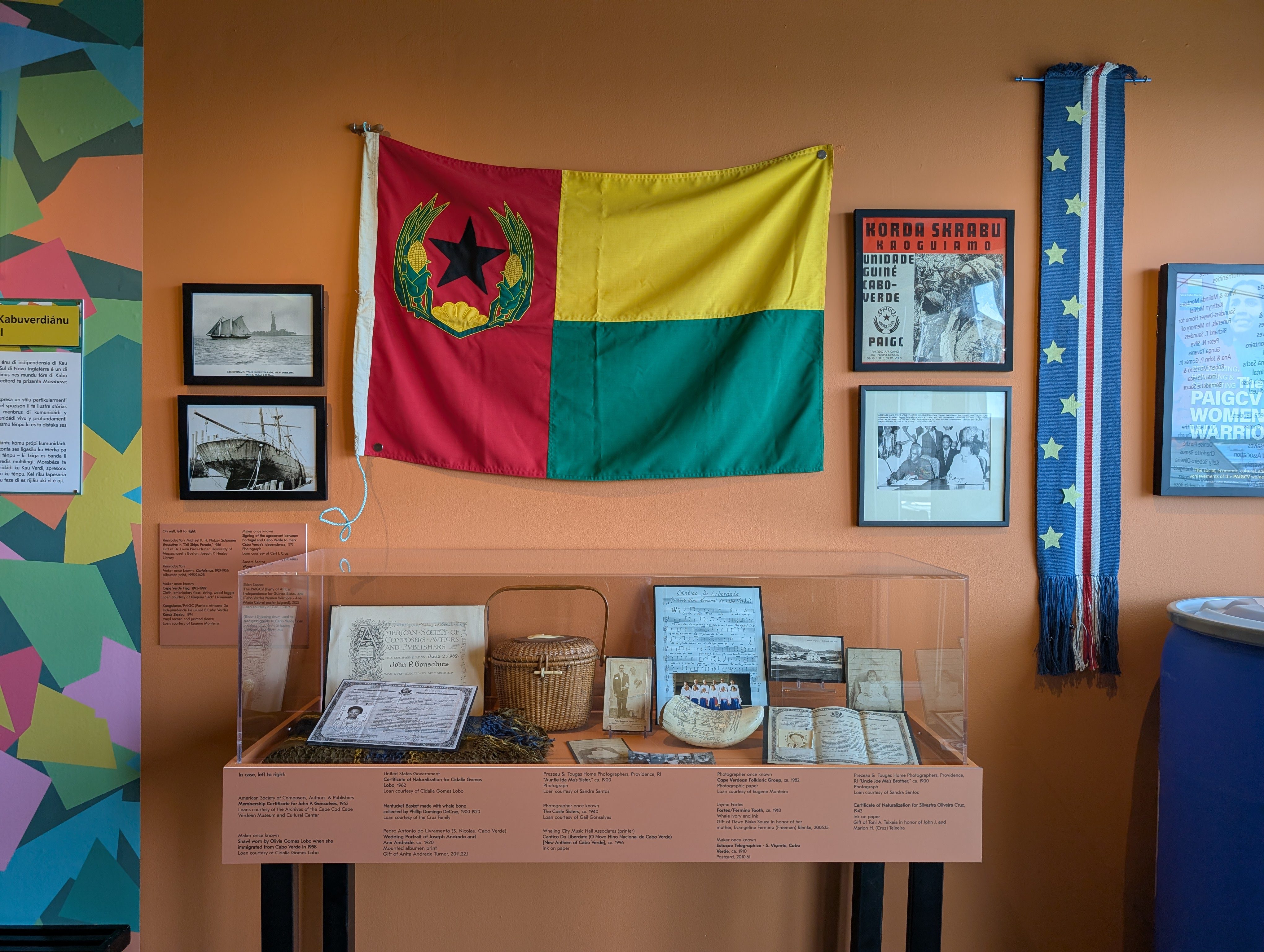 image001 Exhibit display with Cape Verdean flag, framed photos, posters, and artifacts in a glass case at the New Bedford Whaling Museum.