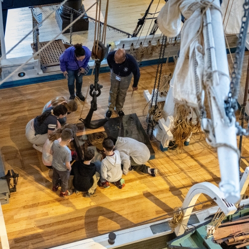 Students and adults on deck of a wooden whaling ship model.