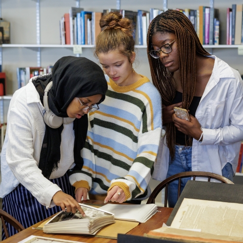 Three students looking carefully at historic documents.