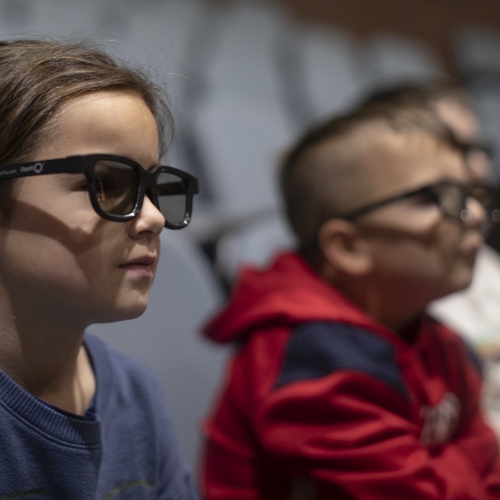 Two students sitting in movie theater wearing 3D glasses.