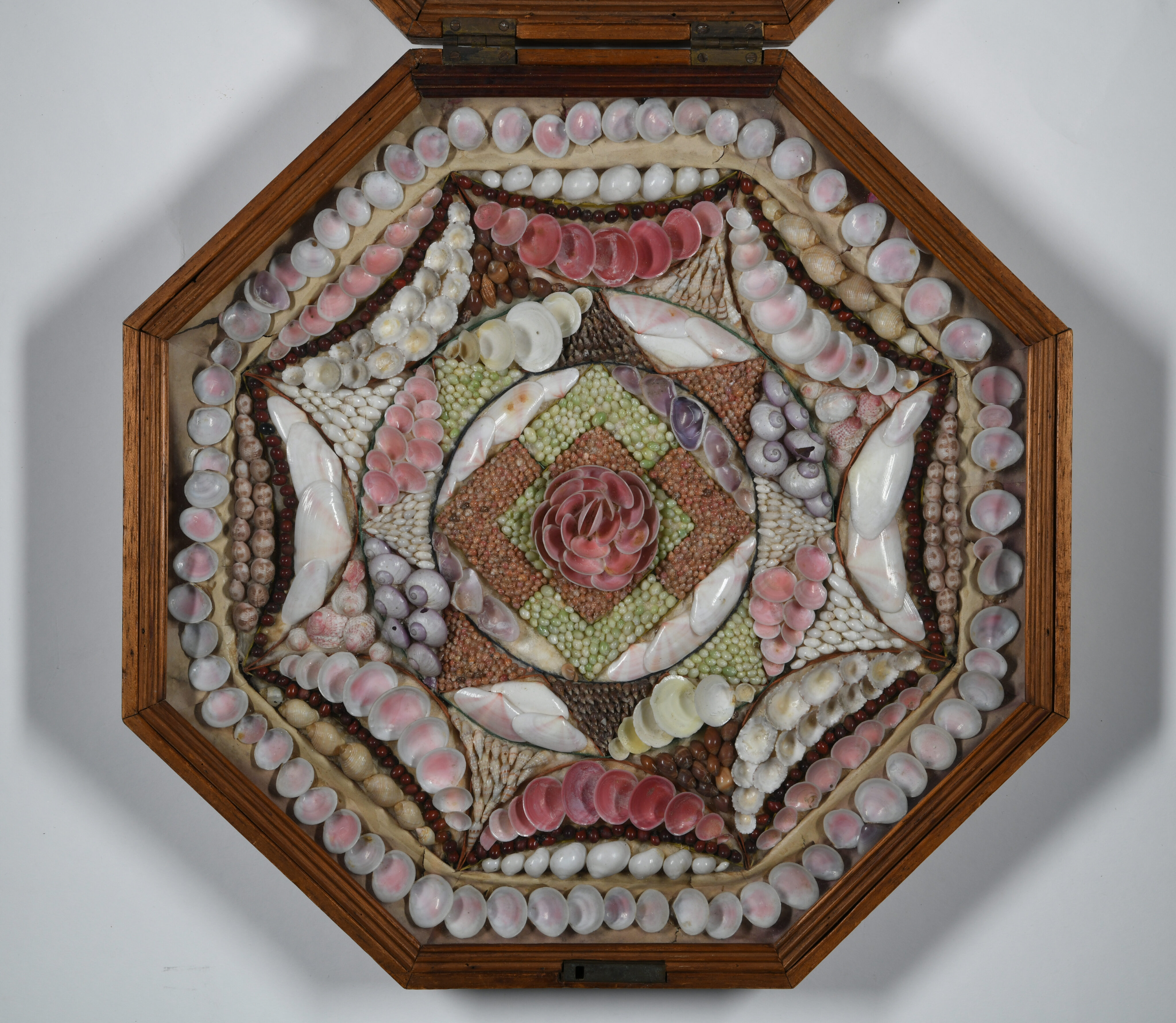 An octagonal wooden shadow box displaying a Victorian sailor's valentine. The artwork features an intricate, star-shaped geometric mosaic crafted from various pink, white, and brown seashells, with a prominent pink shell flower design at the center.