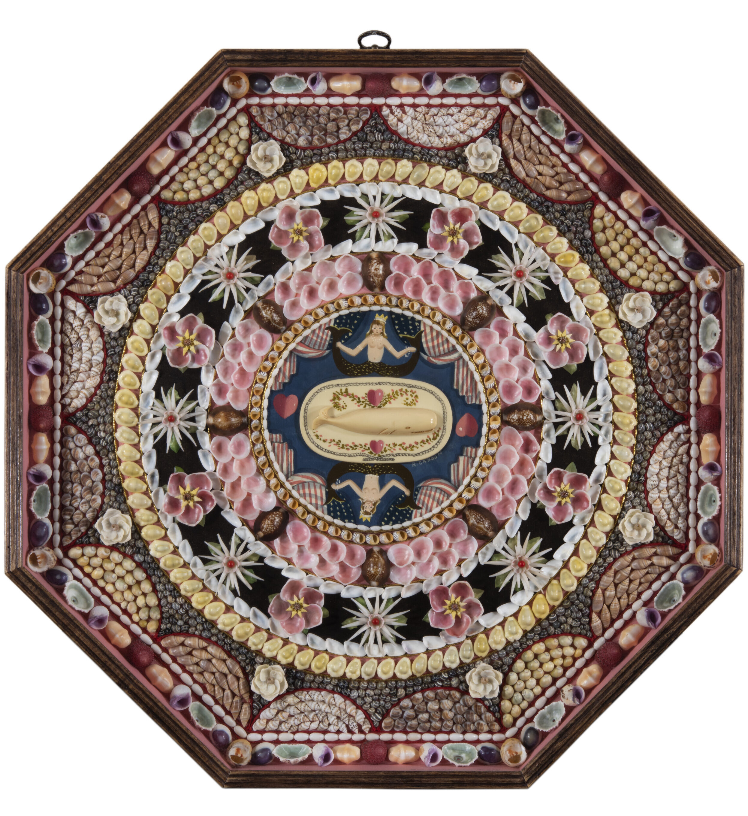 An ornate octagonal shadow box featuring an intricate Victorian sailor's valentine made of shells. The center contains a carved whale and two mermaids on a blue background. This is surrounded by concentric, complex patterns of various shells, including pink, white, and yellow varieties, arranged in floral and geometric designs on a black background.