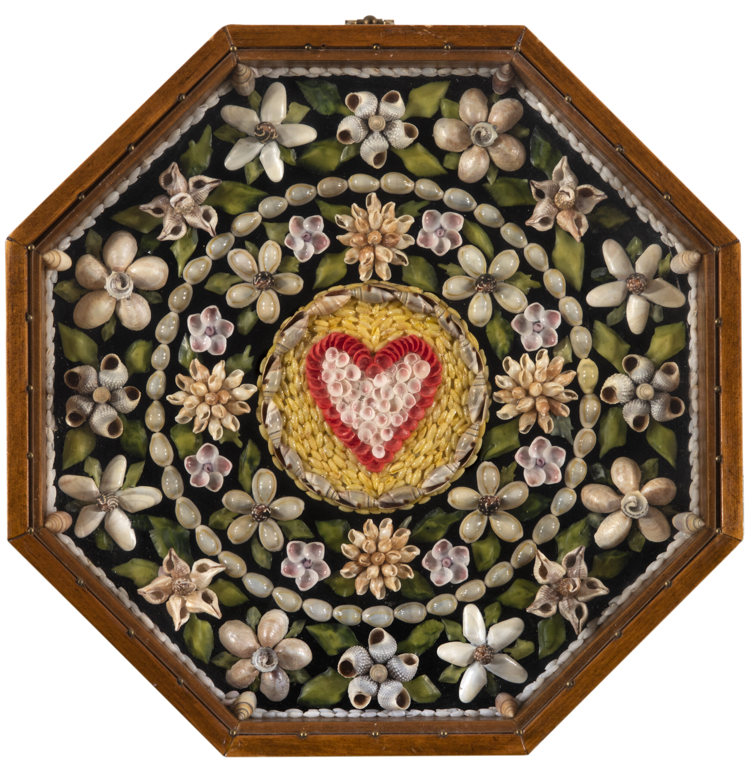 An octagonal wooden shadow box featuring an intricate mosaic made of seashells. The center displays a heart shape crafted from small red and white shells, surrounded by a yellow field. This is encircled by a pattern of various white shell flowers and green shell leaves arranged on a black background.